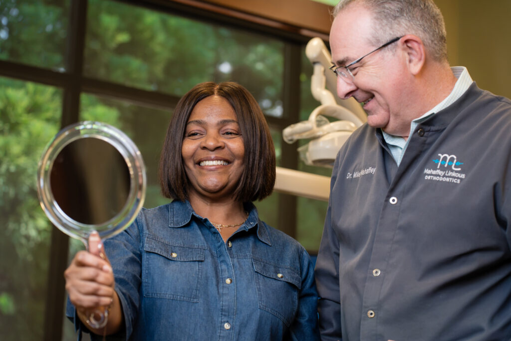 Dr. Mike Mahaffey smiling beside an adult patient as she checks her new smile in a hand mirror in the treatment area at Mahaffey Linkous Orthodontics