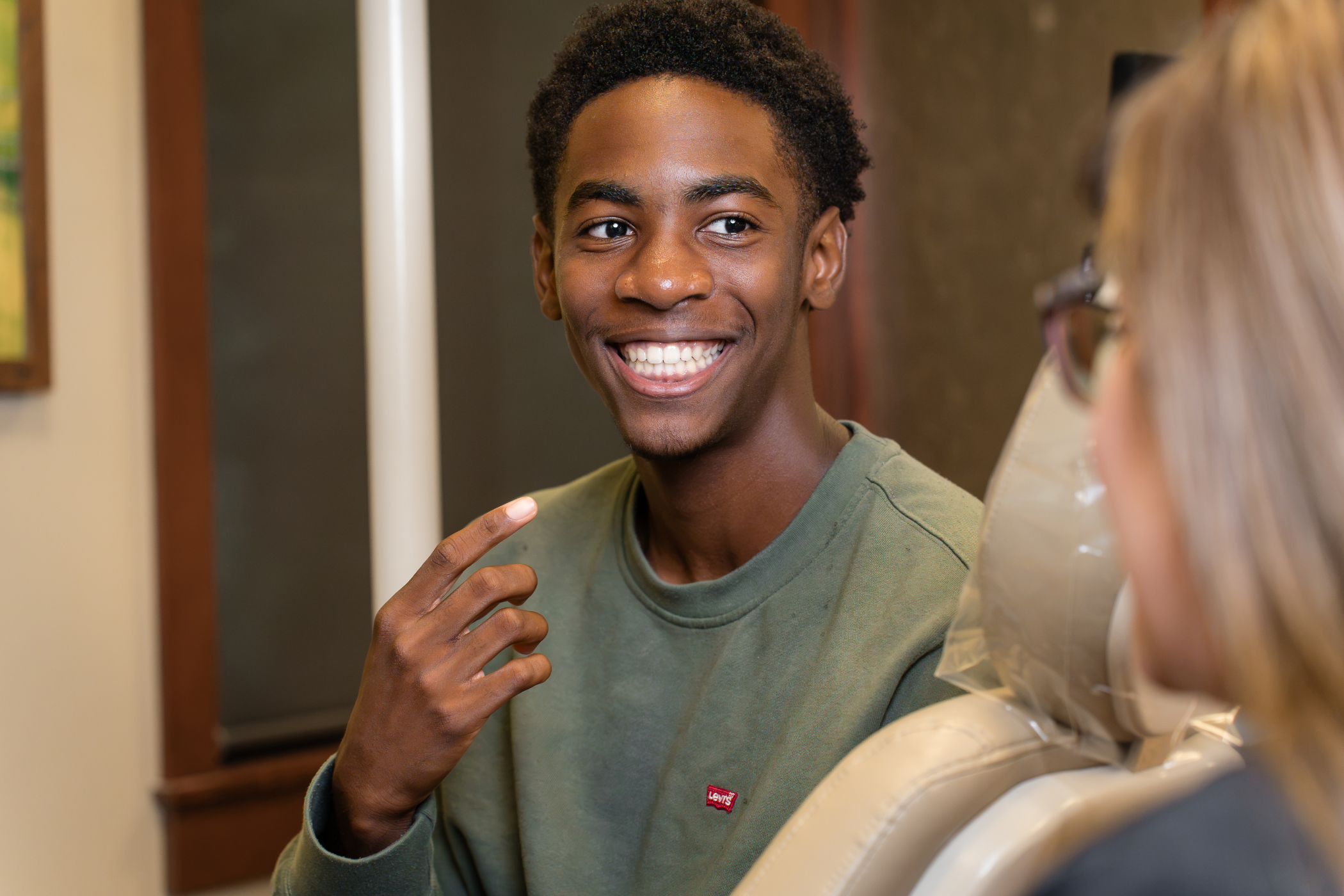 Smiling teen patient in a green sweatshirt sits in a treatment chair and talks with a team member at Mahaffey Linkous Orthodontics in Peachtree City, GA, showing off his straight smile.